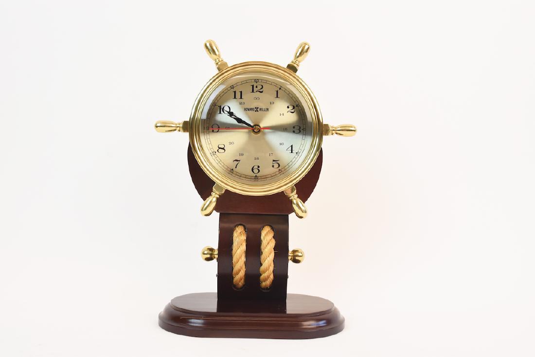 Howard Miller Maritime Ship's Wheel Clock: Howard Miller maritime ship's wheel clock. Brass ship's wheel on mahogany stained wood base with nautical rope detail. Model No. 613467. Serial No. H94008. This clock is made in Taiwan and stands 12"