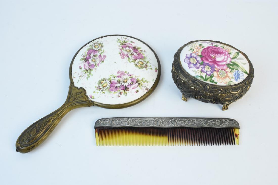 Victorian Style Ladies Vanity Items: A set of vintage porcelain vanity items with floral transfer repousse brass tone handles. The set includes a hand mirror, and a comb. Also featured is a music box that opens to reveal a small area for
