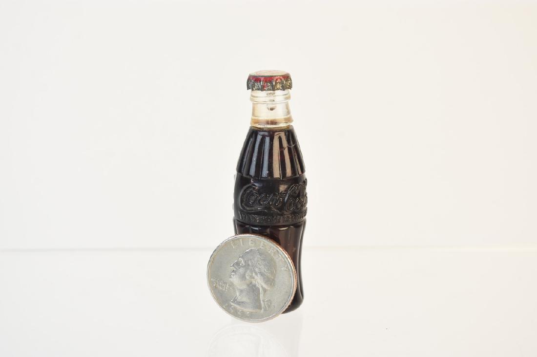 1950s Coca-Cola Miniature Bottle Lighter: A 1950s Coca Cola miniature bottle lighter. The bottle opens at its center to reveal the lighting mechanism. There are some smudges and some dust build up to bottle. Unable to be tested because no flu