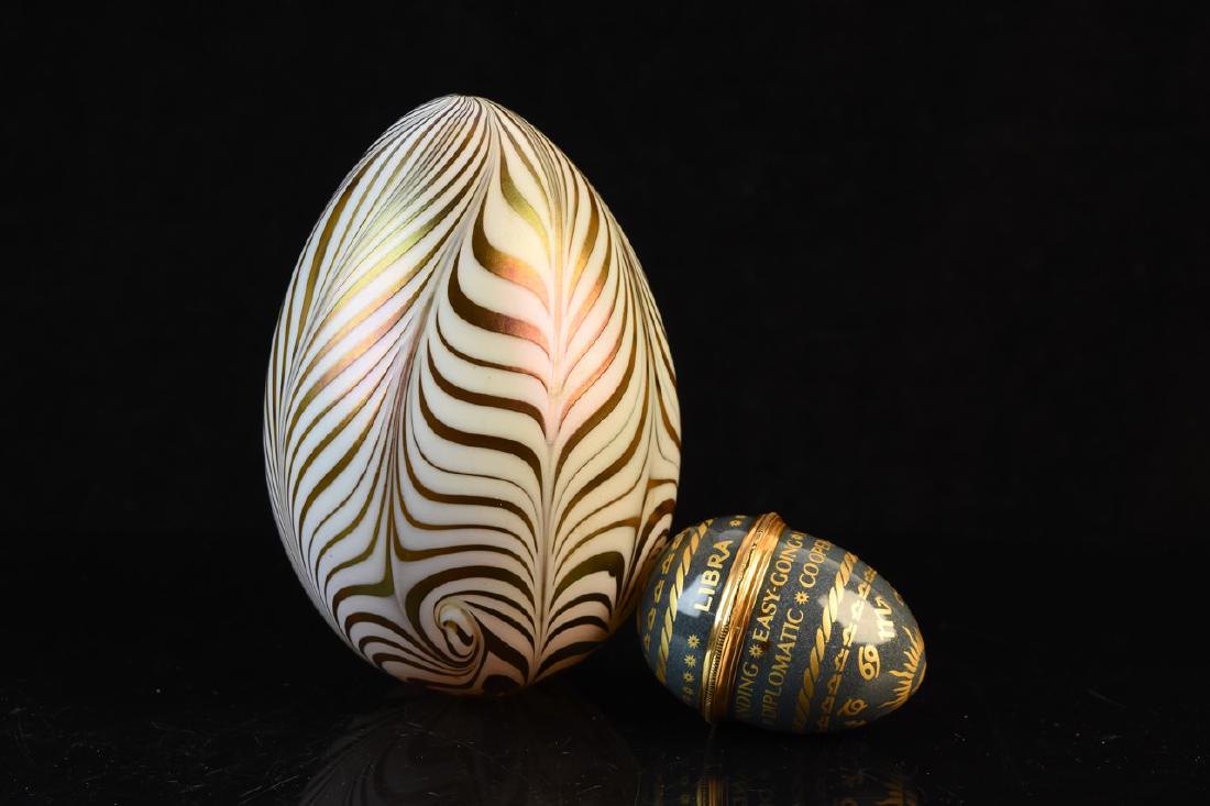 Halcyon “Libra” Enameled Trinket Box Egg & Art: A pair of decorative eggs including one Halcyon Days enamel box “Libra” egg. Also featured is a gold tone and white art glass swirl egg. Light surface scratches to items. Largest egg measures appr