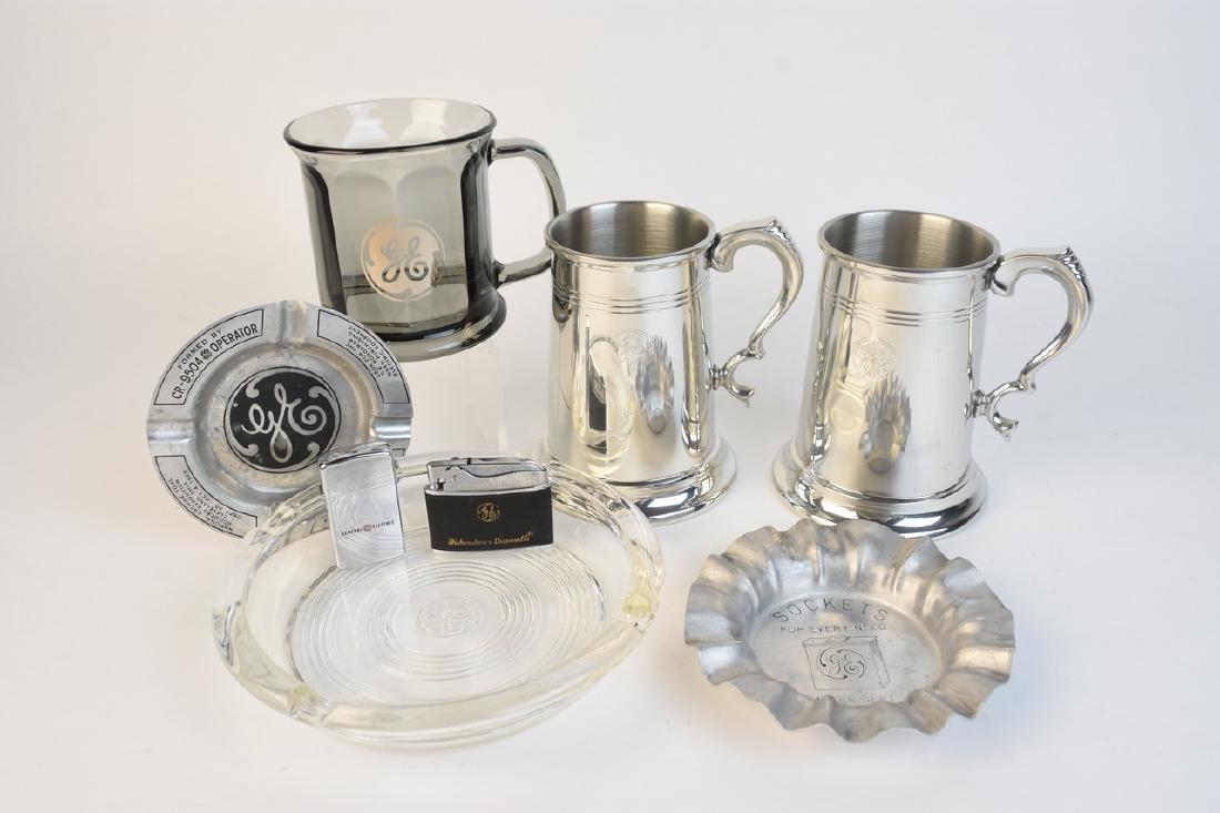 General Electric Tobacciana & Jostens Tankards: General Electric Tobacciana and mugs. Clear glass ashtray with GE logo, 7 " diameter. Scratches and chips where cigarette rests. Two tin GE ashtrays "Sockets for Every Need, Meter Dept" and National M