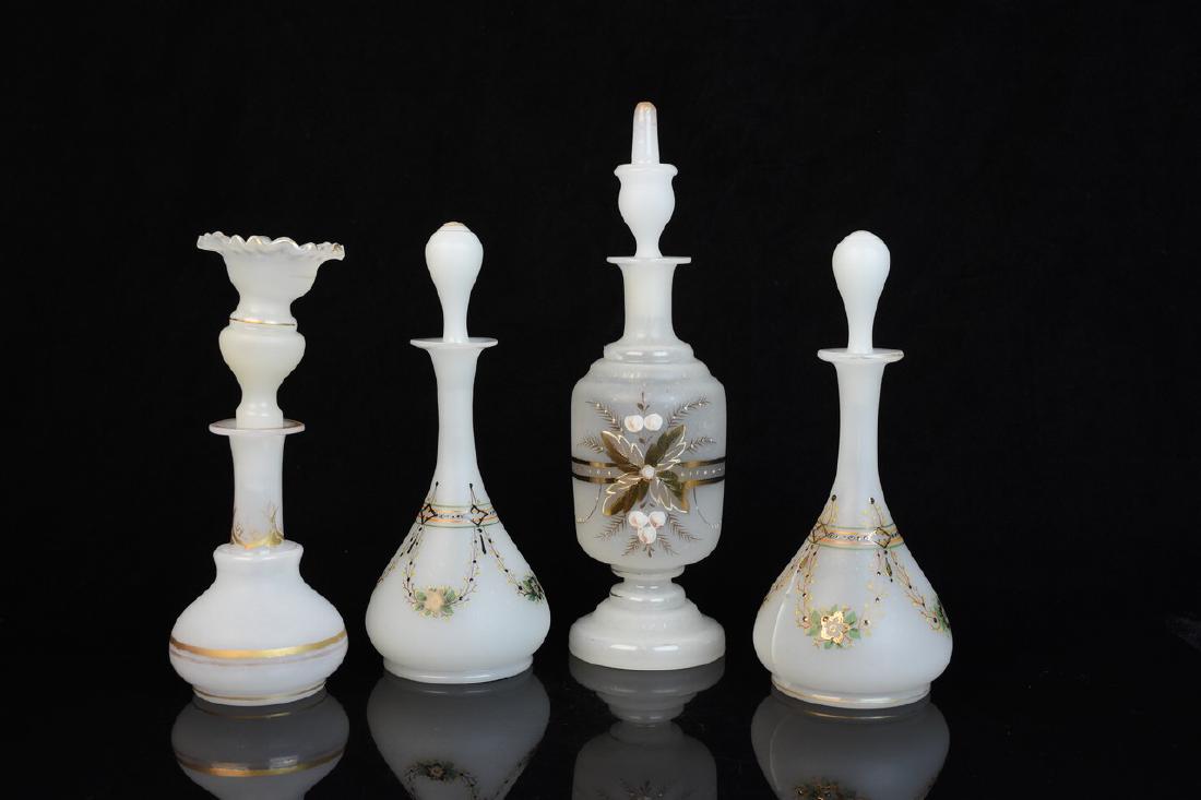 Hand Painted Glass Perfume Bottles: A selection of four hand painted white opaline perfume bottles with intricate hand painted details and removable stoppers. One shows a large crack at its side; one stopper is chipped; loss of paint an