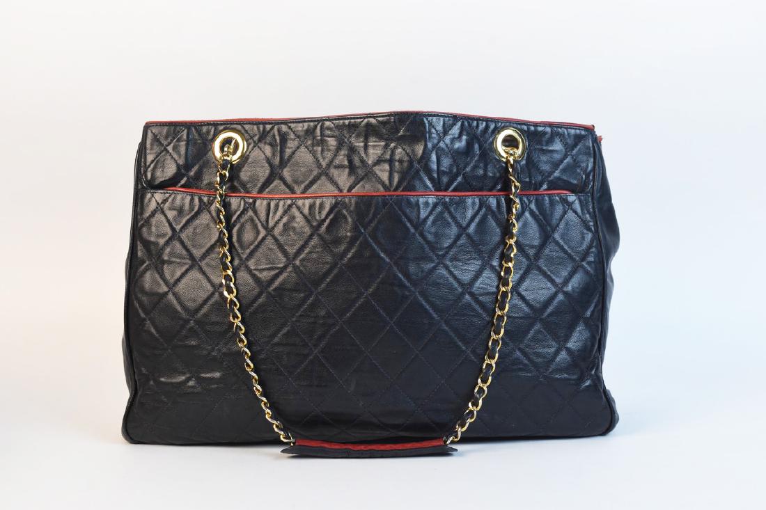Chanel Quilted Lambskin Tote Bag: A Chanel tote in a black quilted pattern accented with red trim. Purchased in the early 1980s at Lou Lattimore of Dallas. Drop length measures approximately 10"; bag measures 11" H x 15.5" W x 4" D. E