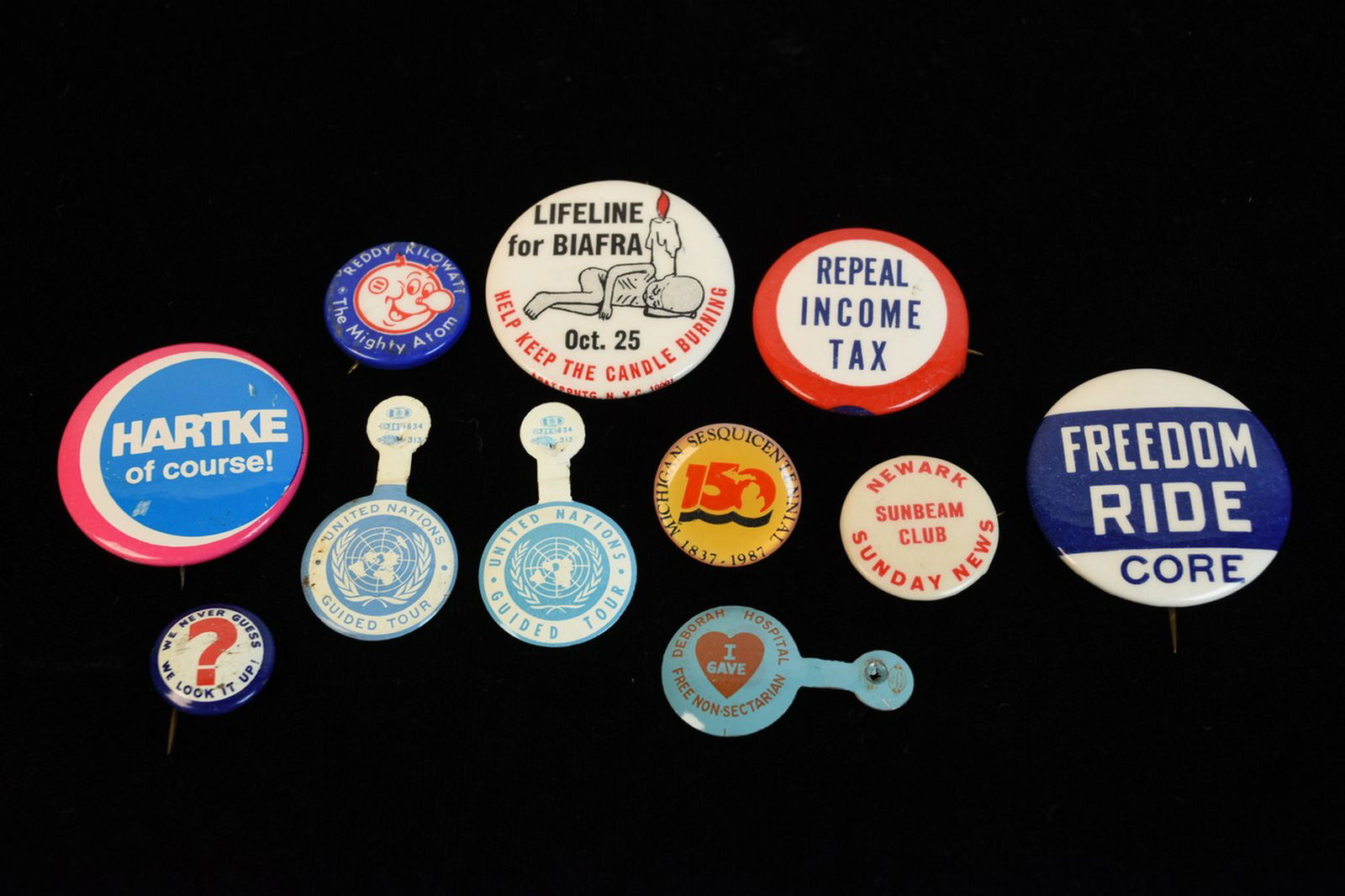 Assorted Vintage Buttons: An assortment of vintage pin back buttons including one that reads "Freedom Ride Core" from the 1960s Civil Rights Movement. Other buttons and tin tabs include "We Never Guess, We Look it Up"; "Newark
