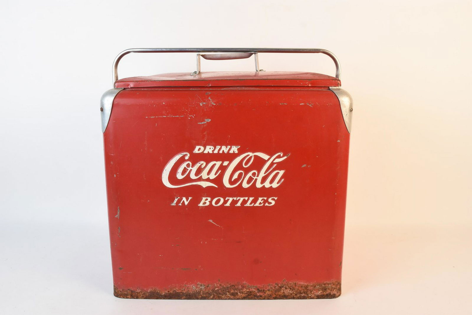 1950s Coca Cola in Bottles Metal Ice Chest: A red metal ice chest from the 1950s marked "Drink Coca Cola in Bottles" to the front. Includes removable lid and pivoting side handle. Also include side bottle opener and a drain. Heavy rust especial