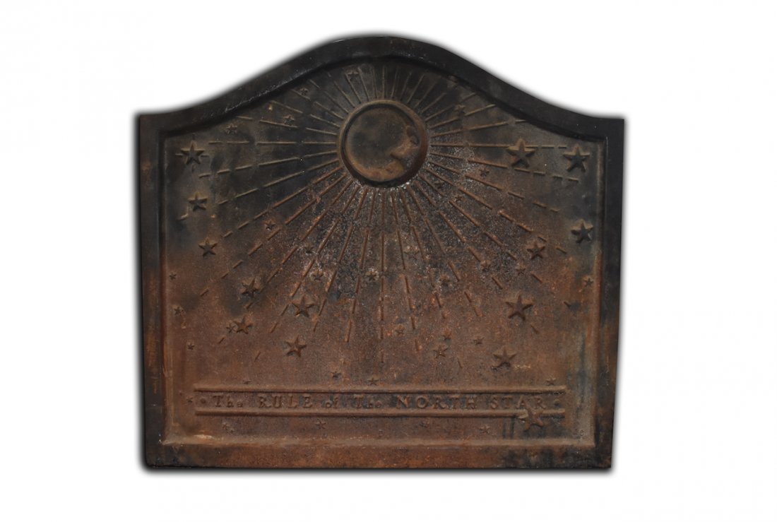 Antique Cast Iron North Star Fireback: An antique cast iron fireback for position against the back of a hearth. It features a scrolled top and a relief design of a sun with multiple stars. Lettering towards its bottom reads "The Rule of th