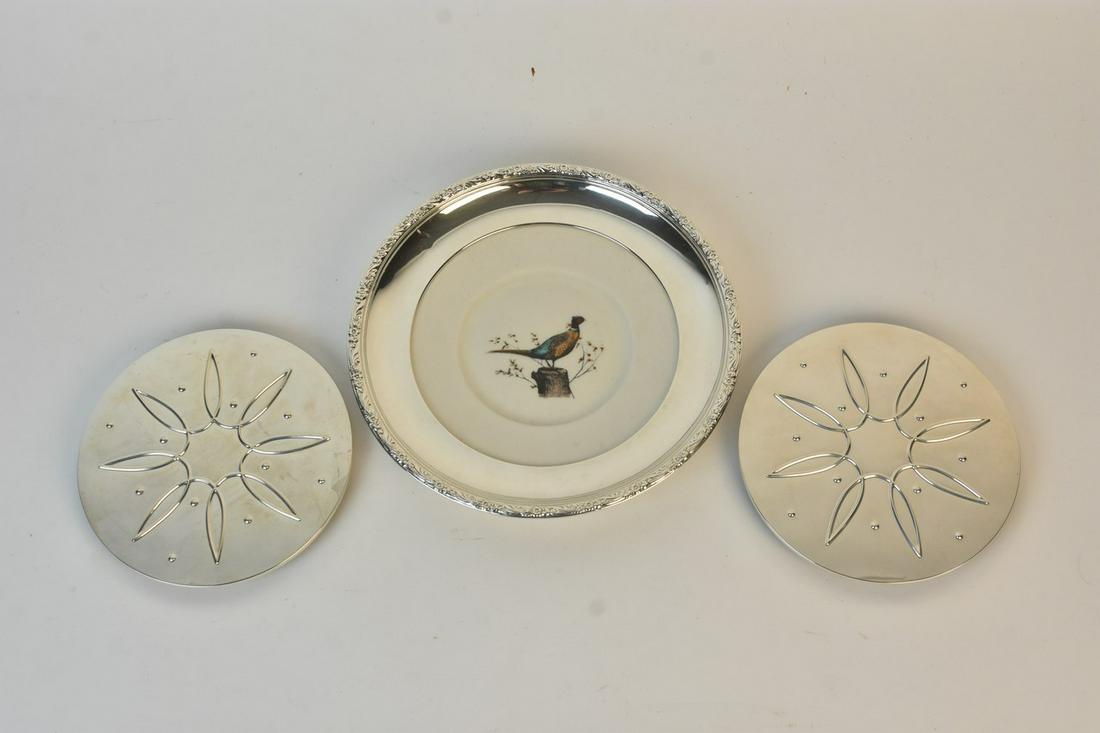 Sterling Trivets and Plate: A trio of sterling silver items including two Towle #09 trivets. Also included is a Frank M. Whiting porcelain Pheasant plate with a collar marked Sterling. The plate measures approx. 9.5" in diameter