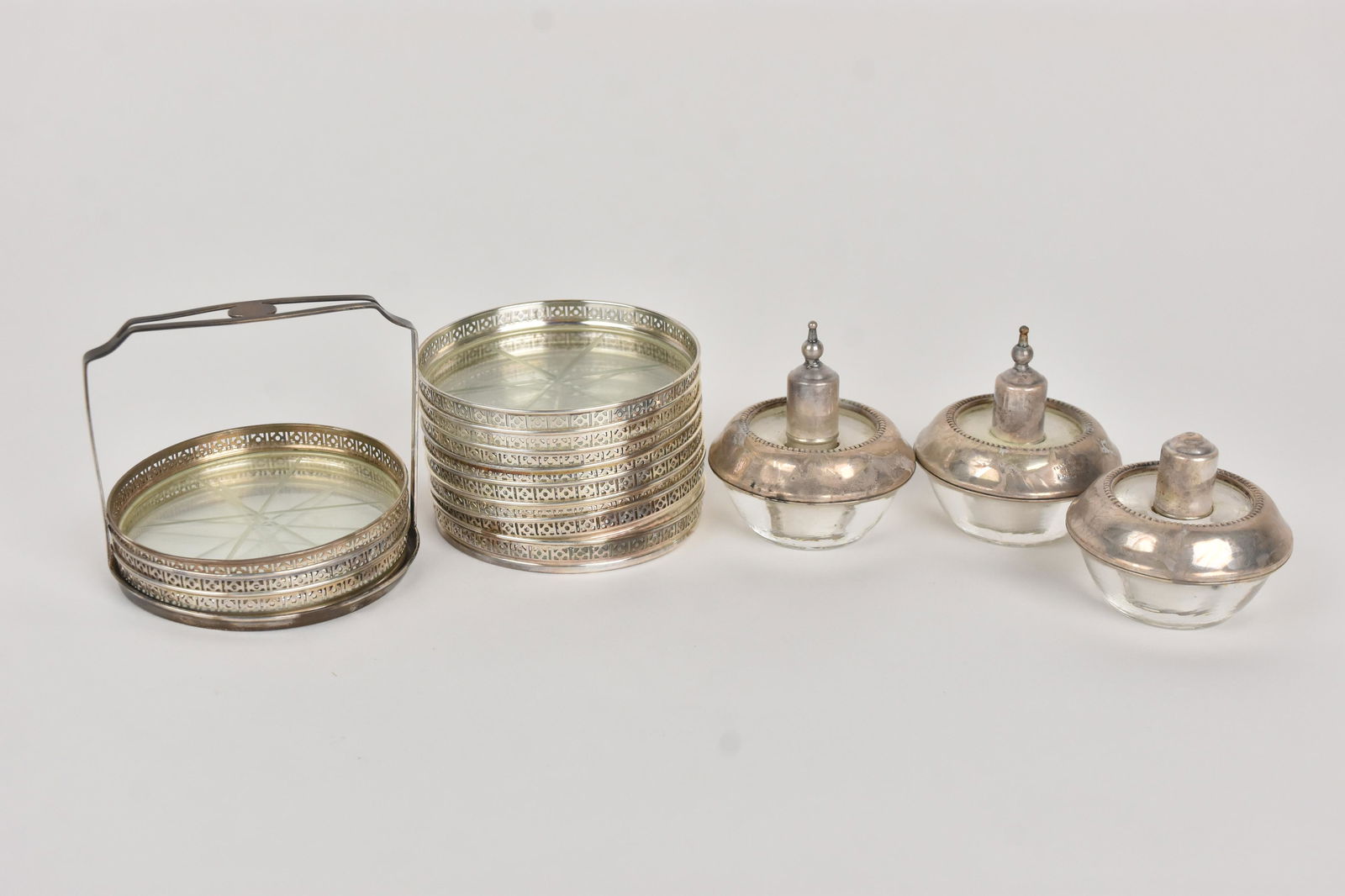 Sterling and Glass Oil Burners and More: A trio of sterling and glass oil burners with a stack of silver tone and glass coasters. The oil burners are marked "Frank M. Whiting Sterling." Tarnish present. Please Note: Scheerer McCulloch Auctio