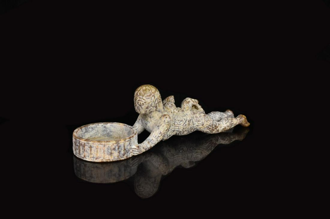Asiatic Carved Soapstone Figure: An Asiatic (Chinese?) carved figurine featuring taotie style carvings throughout; comprised of soapstone. The figure depicts a woman laying on her stomach holding a bowl with her arms outstretched. Ma
