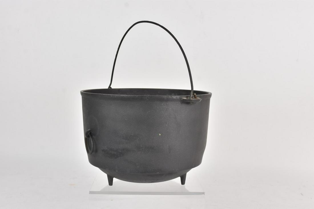 Vintage Cast Iron Cauldron/Kettle: A vintage cast iron kettle or cauldron with bail handle at top and two handles to its sides. Rests on three feet. Measures approx. 7" H x 10" W. Rust and loss of finish to interior; some interior debr
