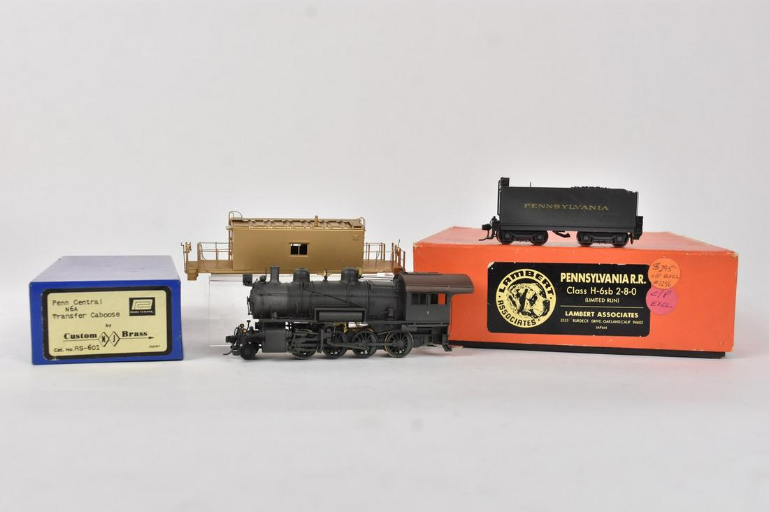 (2) Brass HO Scale Trains: A pair of brass HO scale trains in original packaging. Includes a Custom Brass Penn Central Caboose; and a Lambert Associates Pennsylvania H-6sb 2-8-0. Light shelf wear to packaging. Please Note: Sche
