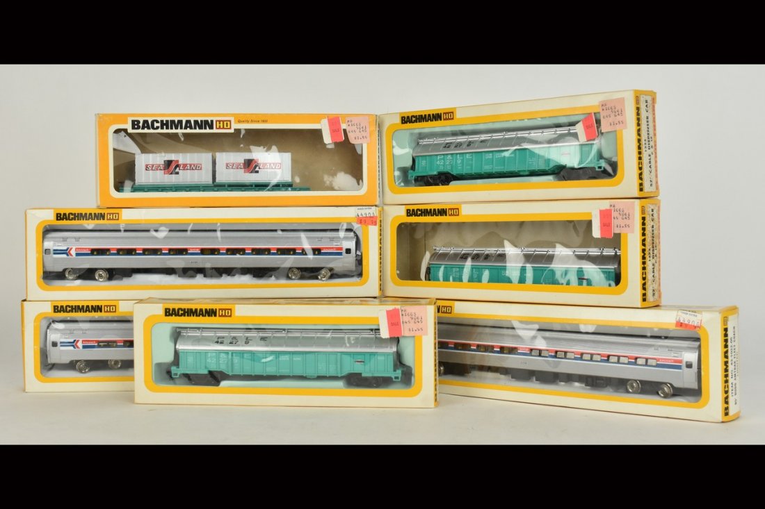 (7) Bachmann HO Scale Train Cars: A collection of seven Bachmann HO scale train cars in original packaging. Includes cable dispenser car, flat car w/ load, Amtrak Fleet Coach cars; and more. Shelf wear and damage to packaging; retail