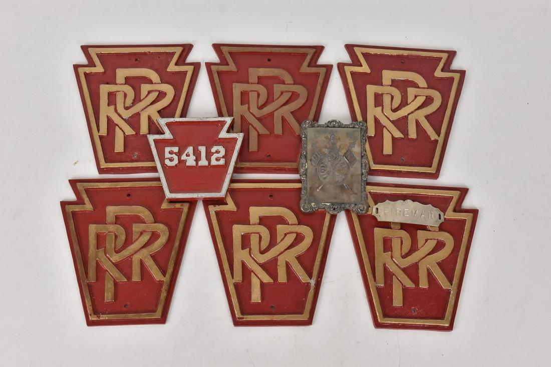 Pennsylvania Railroad Metal Plaques & More: A collection of six PRR Pennsylvania Railroad metal plaques with circular piercings for hanging at its top and bottom. Also included is a "BRRT" metal plate with a filigree border, likely for Brotherh