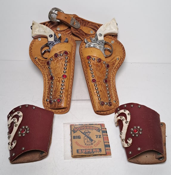 2 Kit Carson Cap Guns, Holster, Cuffs, Caps: 2 Kit Carson cap guns, one gun has damaged grip, Top Hand Togs by Textan of Yoakum holster number 6157, genuine leather, leather cuffs have wear, Mammoth caps, see photos for condition.