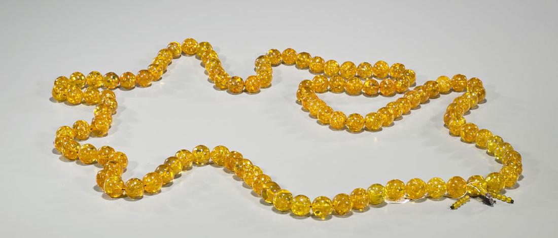 Massive Amber-Like Prayer Necklace: Massive amber-like prayer necklace; composed of many composite beads of spherical form; each of equal size; clasped together with knotted tassel of dark brown coloration; Provenance: From the Collecti