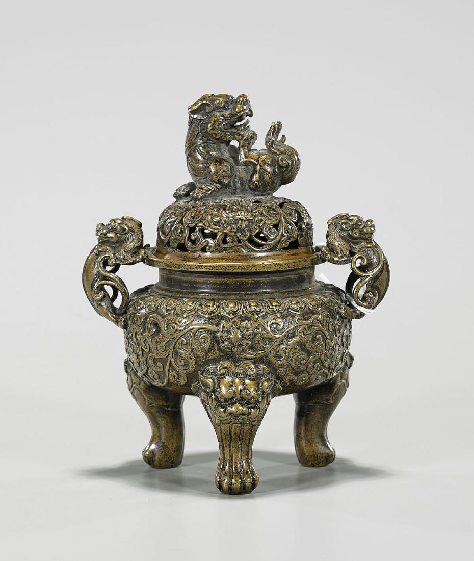 Chinese Bronze Covered Tripod Censer: Chinese bronze covered censer; of squat globular form, set upon a tripod base; with qilong form handles; showing scrolling floral motifs in relief to body; the openwork cover showing pierced designs o