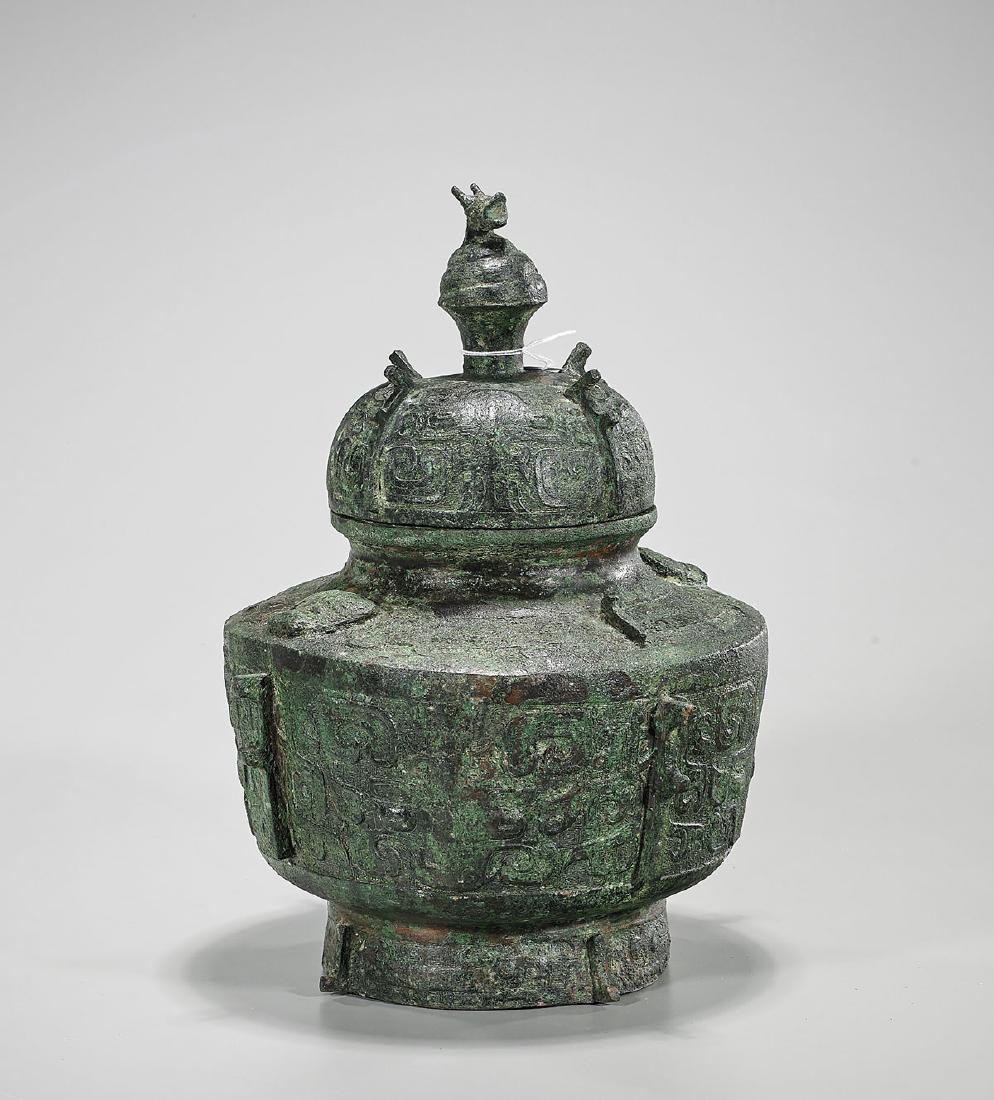 Chinese Archaistic Bronze Covered Wine Pot: Chinese archaistic bronze covered wine pot; with protruding flanges; showing taotie-mask designs in low relief atop an incised diaper patterned ground; with animal form finial; H: 13 1/4" (app