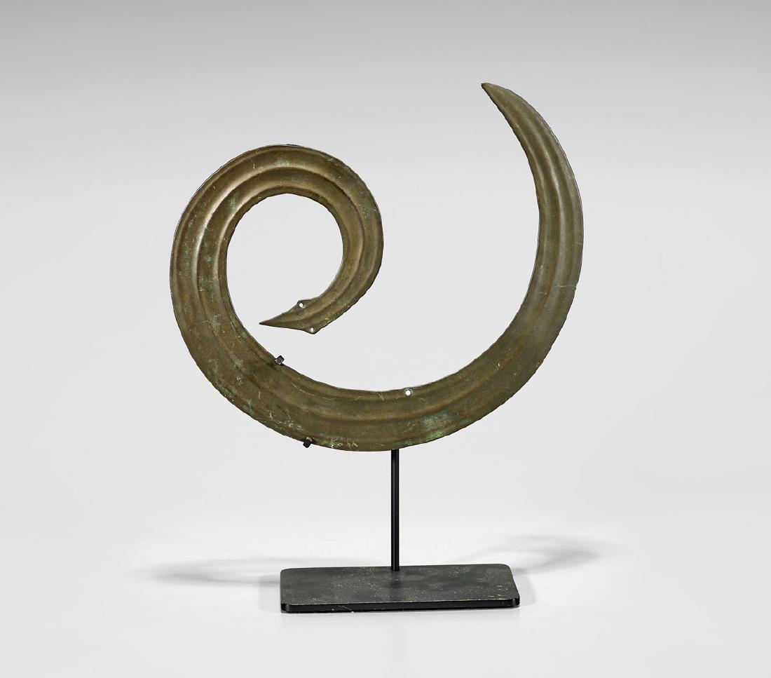 TORAJA BRASS 'SANGGORI' ORNAMENT: Toraja brass sanggori ornament, Sulawesi, Indonesia; of coiled, ridged serpentine form, pierced for use as a headdress crest; L: 9 1/2"; with custom iron stand PROVENANCE Rudi South Oriental Art, 