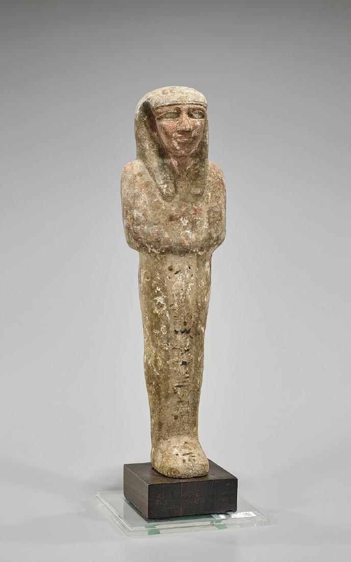 Egyptian Wood Mummiform Figure: Egyptian wood mummiform figure after the ancient; with prominent facial features; framed by a tripartite wig; the body with inscriptions in black; standing atop a wood base, enclosed in lucite case; P