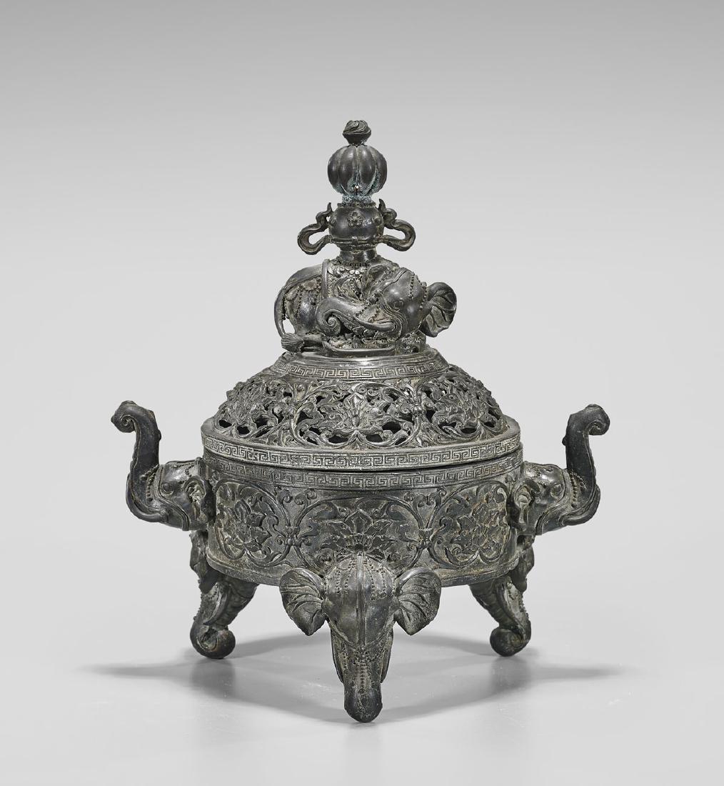 KANGXI-STYLE BRONZE TRIPOD CENSER: Chinese bronze covered tripod censer; the lotus-decorated body with elephant's head handles and feet; surmounted by a reticulated cover with recumbent elephant finial; Kangxi mark to base but 20th