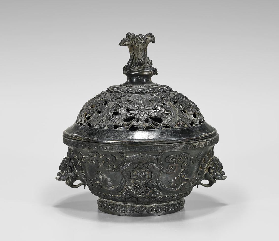 KANGXI-STYLE BRONZE COVERED CENSER: Chinese bronze covered censer; elaborately cast with emblems and lotus motifs; the body with mask handles, and the reticulated cover with wave-form finial; Kangxi mark but 20th Century; H: 9 3/4" 