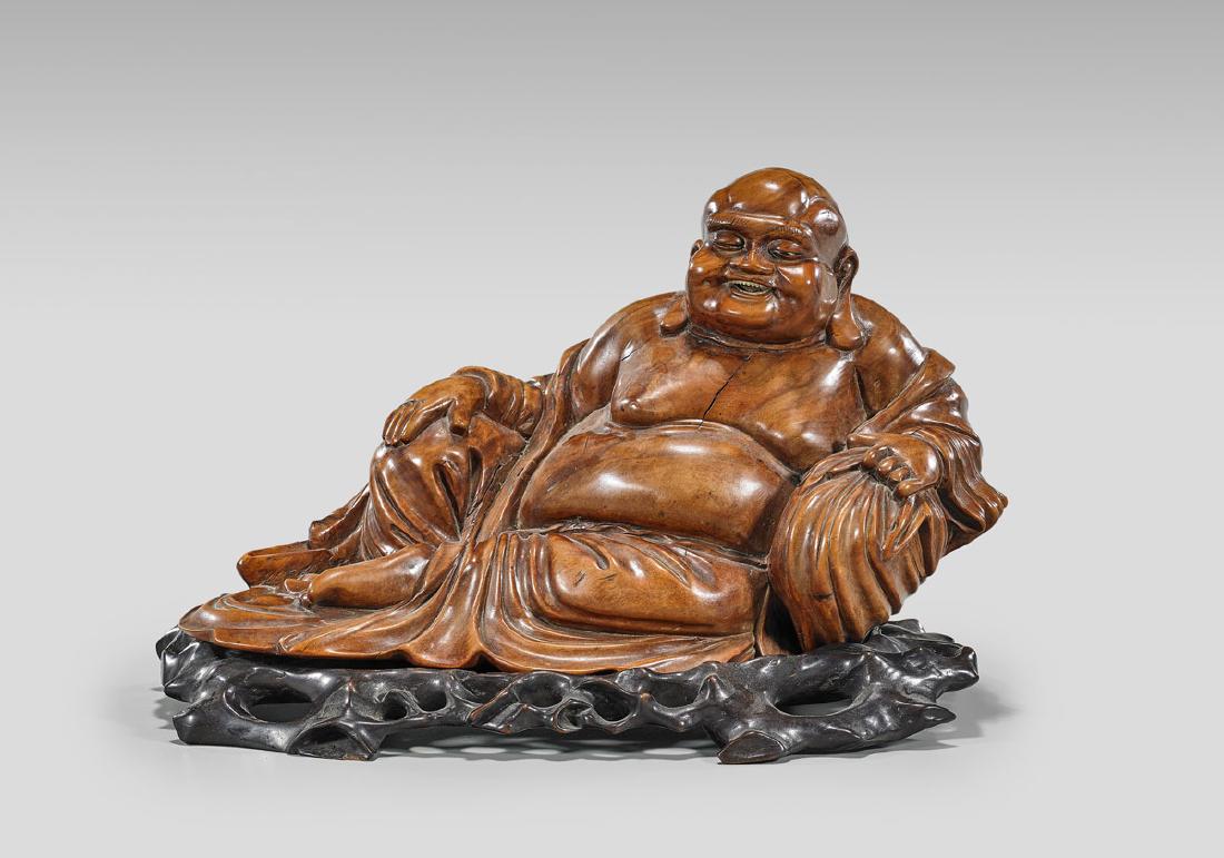 CARVED WOOD FIGURE OF BUDAI: Chinese carved wood reclining figure of Budai; L: 14" (approx.); wood stand