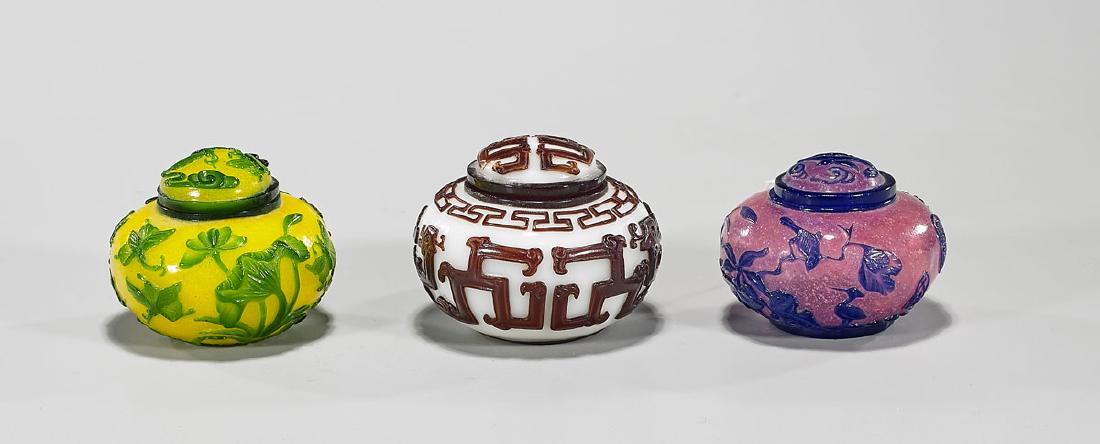 Three Chinese Overlay Glass Covered Jarlets: Three Chinese glass covered jarlets: green overlay yellow; brown overlay white, mark to base; together with blue overlay pink, mark to base; D: 3" (widest, approx.)