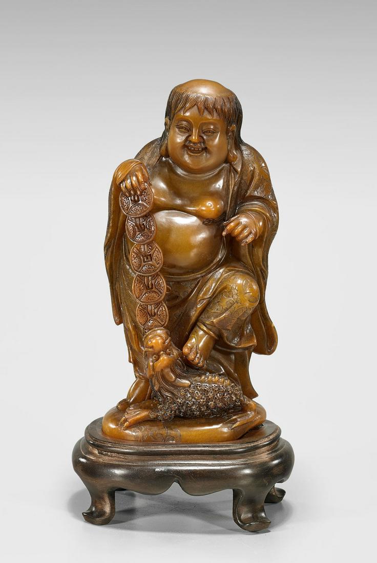 SOAPSTONE FIGURE OF LIU HAI: Chinese carved soapstone figure of Liu Hai; holding coins and standing atop Chan Chu; H: 7 3/4"; wood stand