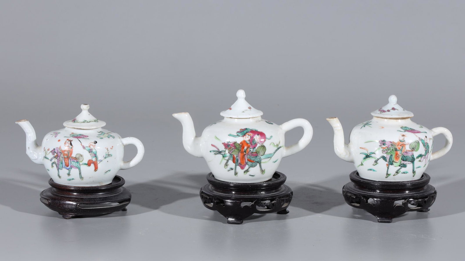 Three Chinese Famille Rose Enameled Porcelain Teapots: Three Chinese famille rose enameled porcelain teapots with gilt detail, four-character mark to base, and each with wood stand; some wear, some losses to gilt and enamel; the largest H 3 3/4" x L 5 3/4