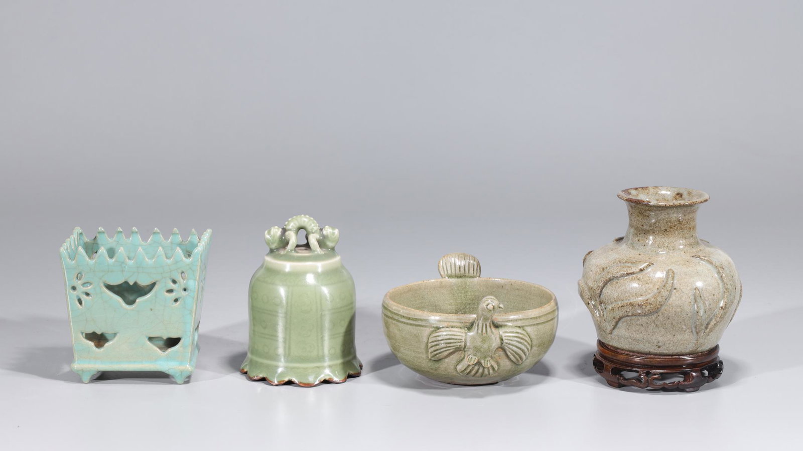 Group of Four Chinese Celadon Ceramics: Group of four Chinese celadon ceramics including vase with molded floral and foliate designs with wooden base, one brush washer with molded handles, one bell-shaped ceramic, one brush holder; overall 