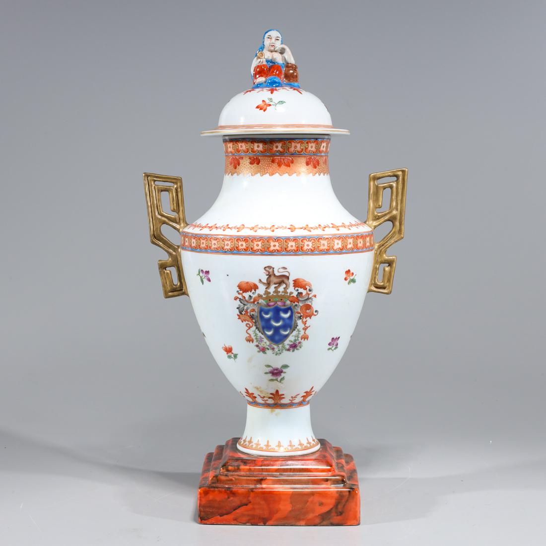 Chinese Famille Rose Enameled Porcelain Covered Vase: Elaborate Chinese famille rose enameled porcelain vase with molded gilt handles and square base, armorial coat of arms and floral designs to body, figural finial to cover; overall good condition, mino