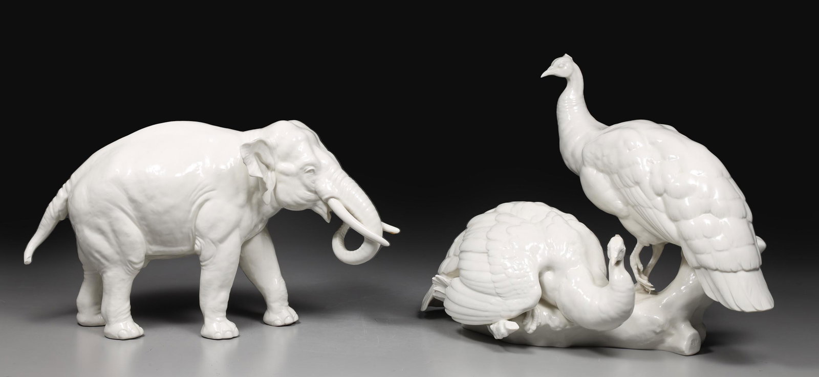 Group of Two Nymphenburg Blanc de Chine Peacocks and Elephant: Group of two Nymphenburg blanc de chine porcelain figures; peacocks on faux bois perch: broken crests, light age wear, light surface wear; elephant: reattached tusk, broken tail, minor age wear, light
