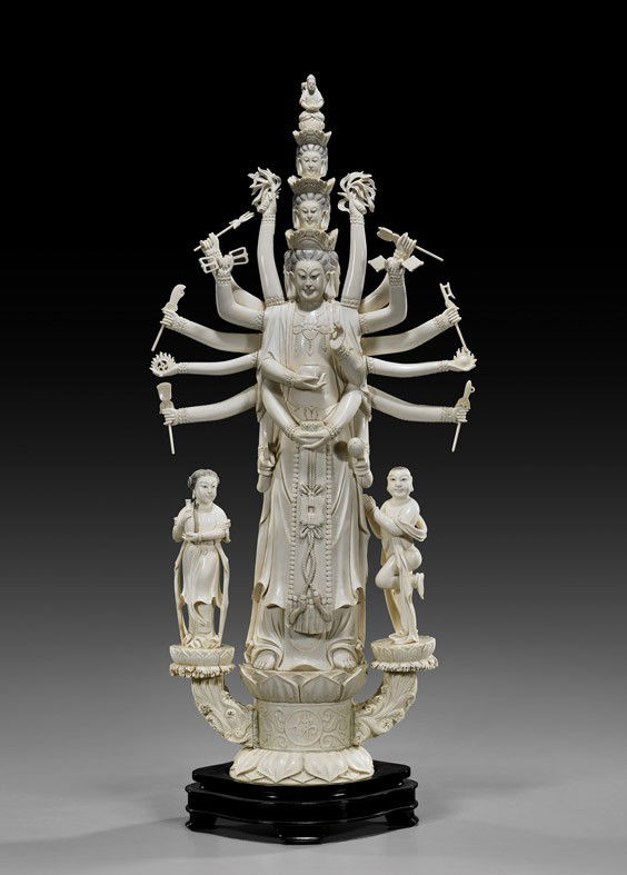 TALL CARVED IVORY MULTI-ARMED DEITY: TALL CARVED IVORY MULTI-ARMED DEITYTall and finely carved, Chinese sectional ivory figure; of a multi-armed and multi-headed deity: holding a ritual object in each hand, the three tiers of heads surmo