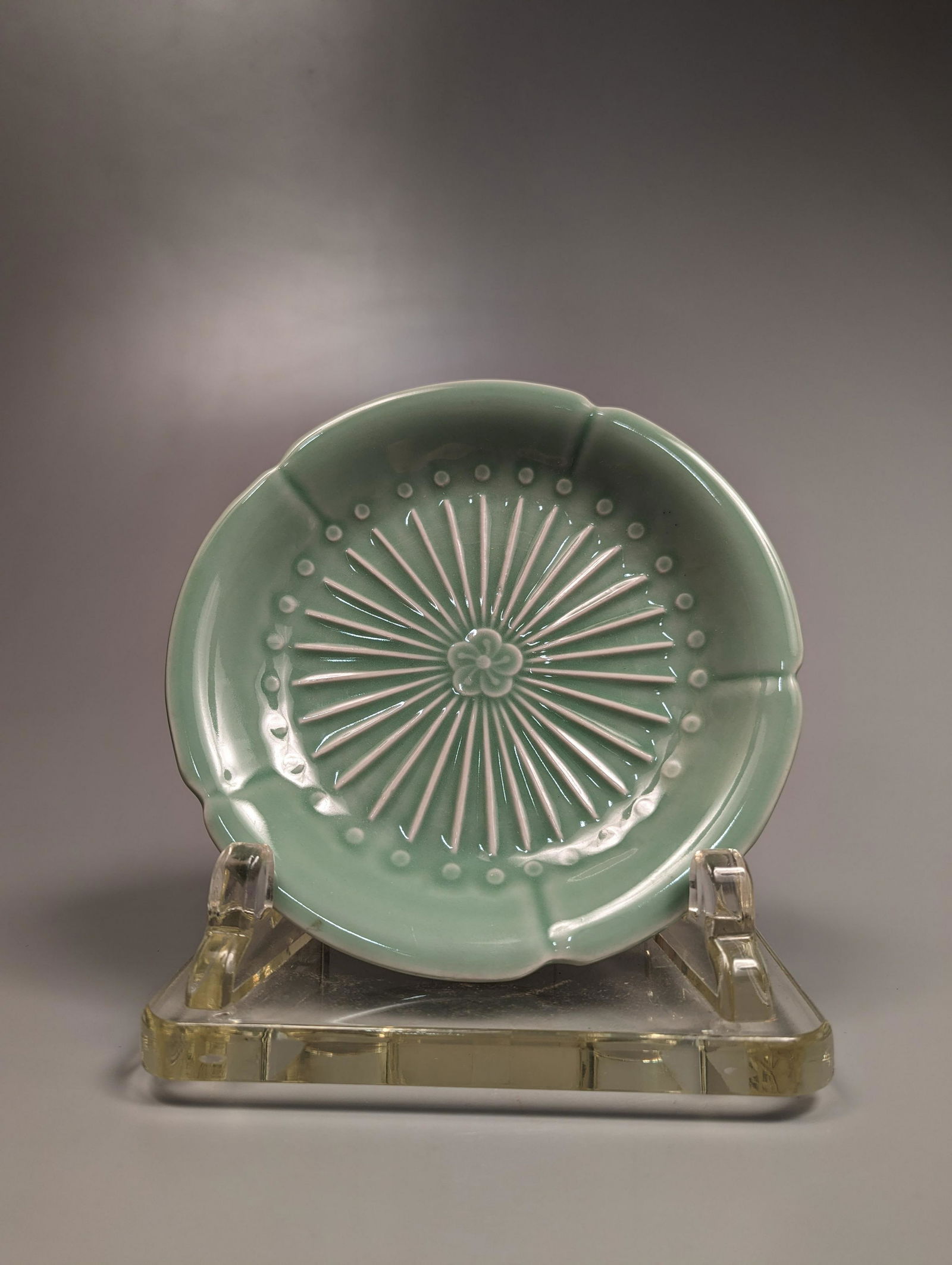 Celadon Plum Blossom Porcelain Dish: Chinese bright celadon glazed porcelain dish; of petaled shape with a singular plum blossom at center in relief, with radiating ribs and prunts; archaic-style sealmark; D: 8 1/2" (approx.)