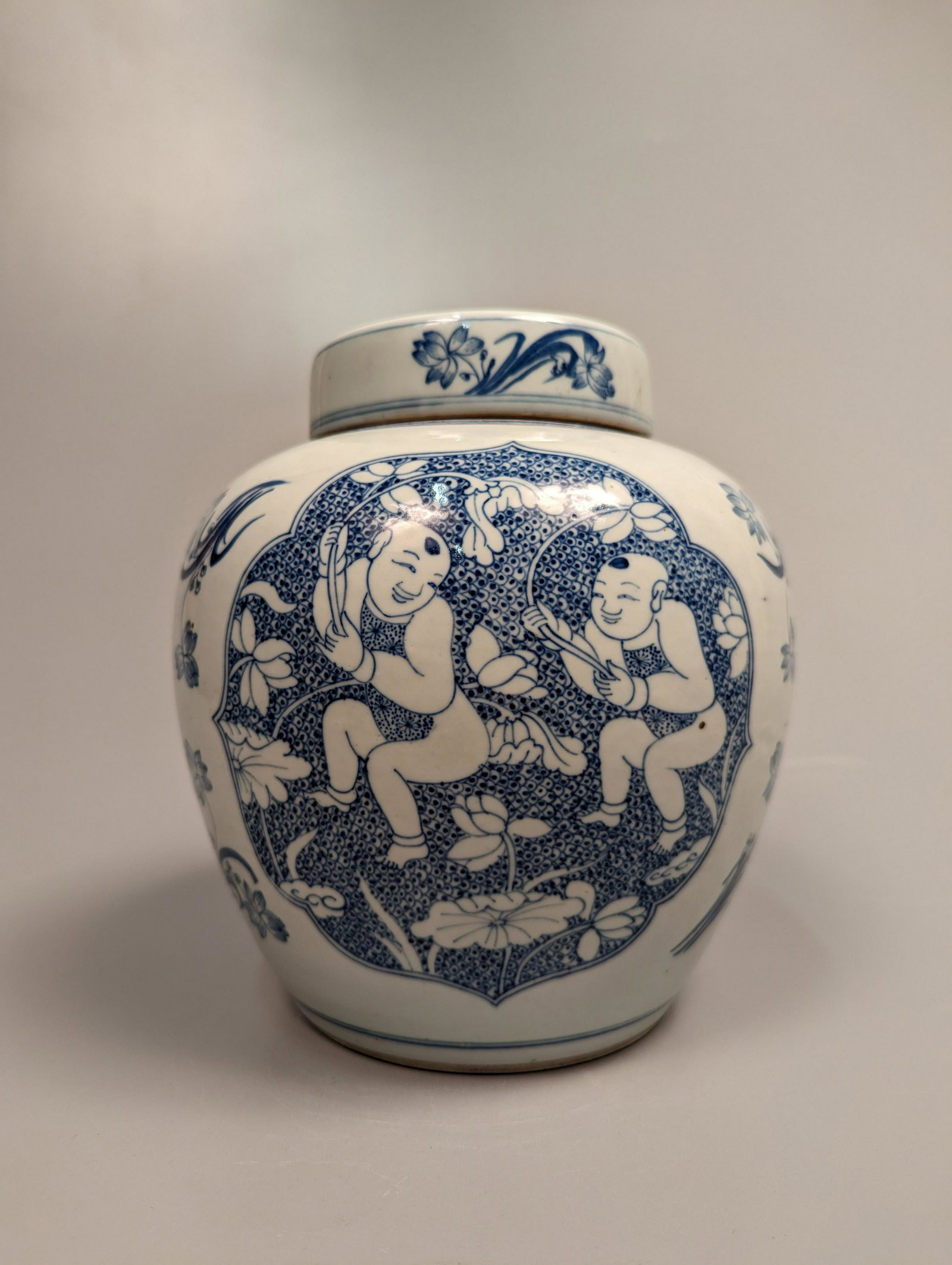 Chinese Blue and White Porcelain Babies Jar: Chinese 19th Century-style, blue and white porcelain ginger jar; decorated with three foliate panels of double baby boys, flanked by scattered lotus; a geometric band to the shoulder; with matching fl