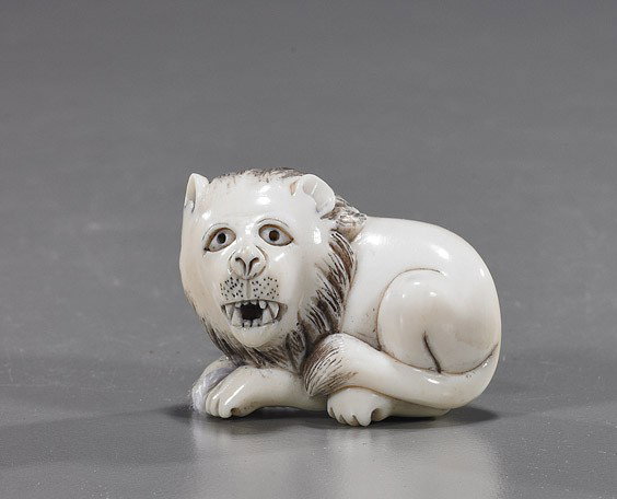 Carved Ivory Netsuke: Lion: Carved Ivory Netsuke: Seated Lion Carved ivory netsuke; of a lion in repose and baring its teeth, inked incised details, signed