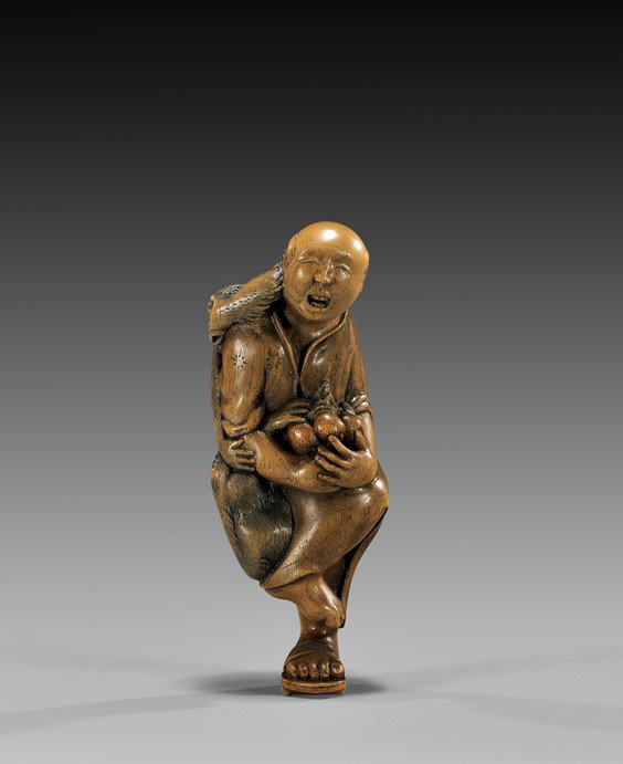CONTEMPORARY WOOD NETSUKE: Monkey trainer: CONTEMPORARY WOOD NETSUKE: Monkey trainer Contemporary carved and lacquered wood figural netsuke; of a monkey trainer (sarumawashi) carrying a lap full of fruit, and standing on one foot with two monk