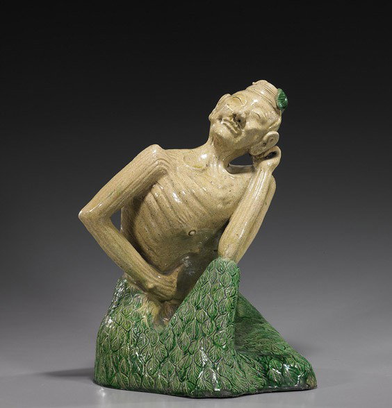 Chinese Glazed Ceramic Buddhist Ascetic: Chinese Glazed Ceramic Buddhist Ascetic Unusual Chinese green and yellow glazed model of a seated Buddhist ascetic; stylized figure wearing a leaf design skirt, possibly Shekwan ware; H: 15 1/2", wood