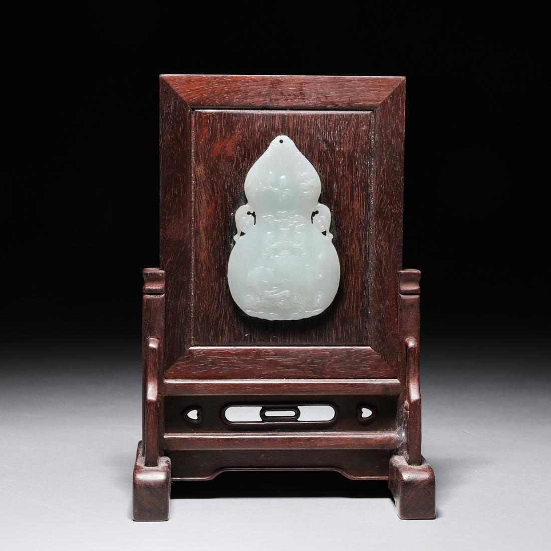 Chinese Carved Jade & Hardwood Miniature Table Screen: Chinese carved mutton fat jade pei mounted on hardwood table screen; the pei finely carved in sharp relief depicting twin figures holding vase with spray of ruyi atop elephants riding clouds with peac