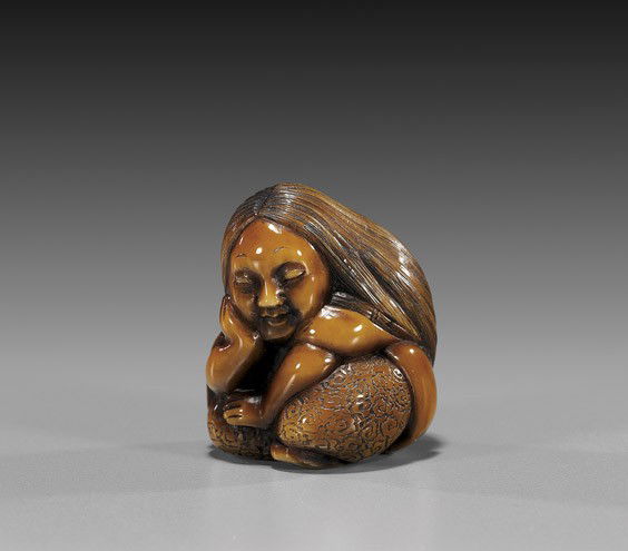 CARVED IVORY NETSUKE: Seated Okame: CARVED IVORY NETSUKE: Seated OkameWell carved and darkly stained, ivory netsuke; of a seated Okame curled into a ball, signed