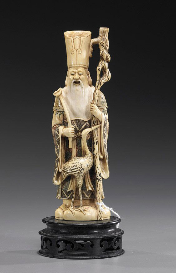 Carved Ivory Okimono: Deity: Carved Ivory Okimono: DeityCarved ivory okimono figure of a bearded deity; standing in scrimmed and polychromed robes and wearing a tall hat, holding a staff in one hand, a ruyi fungus in the other, a