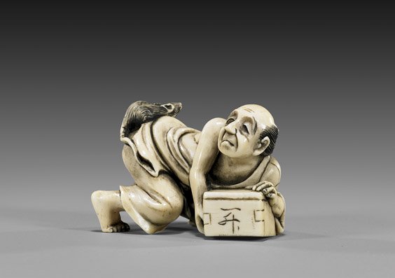 CARVED IVORY NETSUKE: Rat Catcher: 象牙根付 CARVED IVORY NETSUKE: Rat Catcher Carved ivory netsuke; of an unsuccessful rat catcher on his hands and knees, with a rat on his rump, signed Ikkosai(?), early 20th Ce