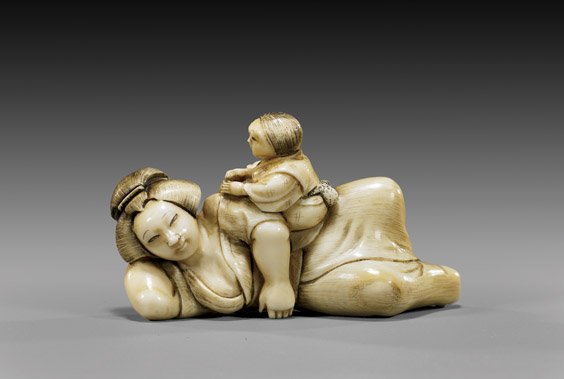 CARVED IVORY NETSUKE: Woman & Child: 象牙根付 CARVED IVORY NETSUKE: Woman & Child Charming early 20th Century carved ivory netsuke; of a reclined woman with a child mischievously playing on her hip, signed Yukihar