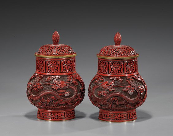 Pair Chinese Carved Cinnabar Lacquer Jars: Pair Chinese Carved Cinnabar Lacquer JarsPair of Chinese carved red cinnabar lacquer jars and covers; each of footed, heavy-bottomed form with panels depicting writhing dragons and with floral motifs