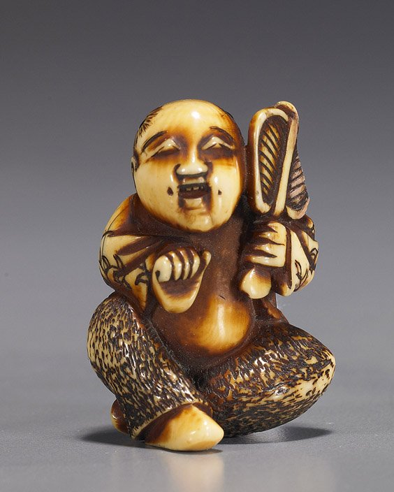 Antique Carved Ivory Netsuke: Boy with Fan: Antique Carved Ivory Netsuke: Boy with Fan Stained and finely patinated, antique carved ivory netsuke; of a seated Chinese boy (karako) holding a fan and with inlays to his head (wear, large chip to f