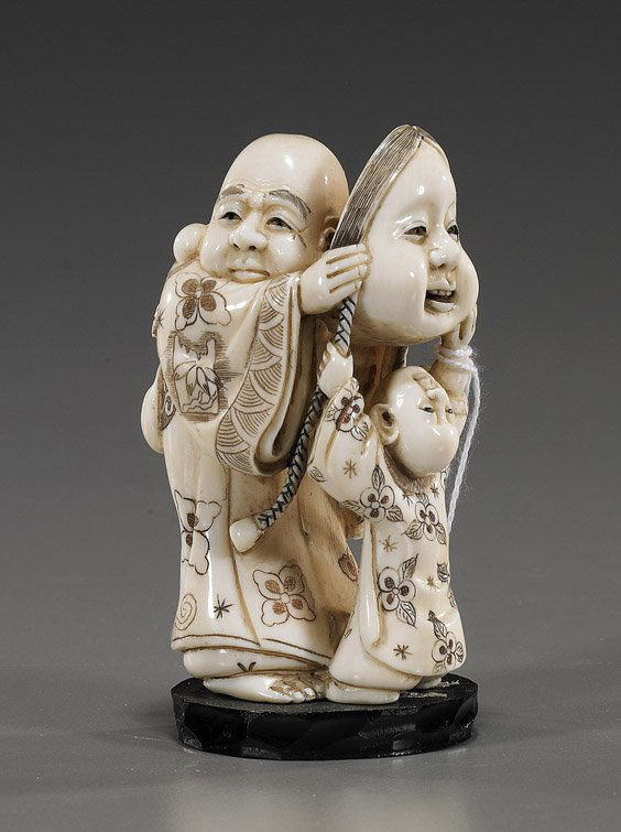 Carved Ivory Okimono: Figure with Mask: Carved Ivory Okimono: Figure with MaskFinely carved ivory okimono; of an aged figure with long ear lobes: standing in floral robes and holding a large mask, and being helped by a boy, attractive scrim