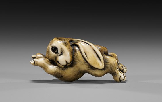 CARVED IVORY NETSUKE: Leaping Rabbit: 象牙根付 CARVED IVORY NETSUKE: Leaping Rabbit Charming and amusing, carved ivory netsuke; of a leaping rabbit, showing fine patination and staining; with inlaid eye, signed in 