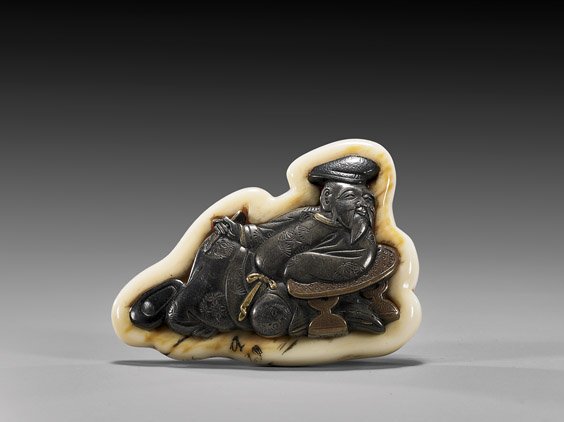 ANTIQUE IVORY KAGAMIBUTA MANJU: 象牙金屬根付 ANTIQUE IVORY KAGAMIBUTA MANJU Highly unusual, antique ivory mounted kagamibuta manju netsuke: with silvered soft metal plaque of a deity or scribe sea