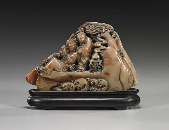 Small Chinese Carved Soapstone Mountain: Small Chinese Carved Soapstone Mountain Small Chinese carved soapstone mountain; depicting a woman and attendant on rockery above waves, one woman in repose beneath pine; L: 6", wood stand