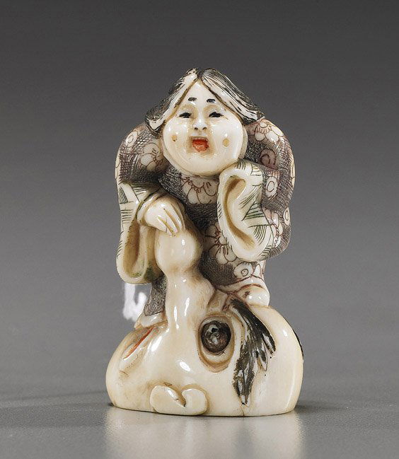 Ivory Shunga Netsuke: Okame & Mask: Ivory Shunga Netsuke: Okame & MaskIvory carved shunga netsuke; parcel-lacquered with Okame standing atop a Tengu mask with "phallic nose", signed (minor chip to back); Provenance: de-accessioned from